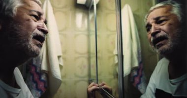 Ayna çerçevesini tutan adam, acı içinde kıvranan yüz, yansımada cevaplar arayan gözler, iç çatışmanın, öfkenin ve çaresizliğin dramatik keşfi.