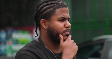 Düşünceli bir ifadeye sahip, eli çenesinde, odaklanma ve kararlılıkla yansıtan ve planlayan, profesyonel ortamda hırs ve problem çözmeyi sembolize eden genç bir siyah adam.