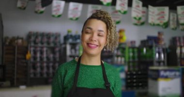 Yerel hırdavatçıdaki kadın, parlak bir şekilde gülümsüyor, renkli boya ve aletlerle çevrili, sıcak ve olumlu bir perakende satış ortamı sergiliyor.