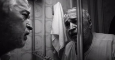 Yaşlı bir adam banyo aynasında yansımasıyla yüzleşiyor. Pişmanlık, yalnızlık ve duygularının ağırlığıyla mücadele ederken gözleri kederle dolu.