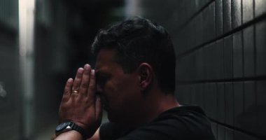 Dar bir sokakta duvara yaslanmış bir adam, başı yukarı eğilmiş, derin acı ve umutsuzluğun yüz ifadesi, üzüntü, duygusal karmaşa ve umutsuzluğu iletiyor.