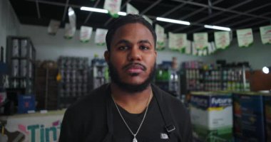 Boyacı dükkanındaki Afrikalı Amerikalı adam elinde boya kutuları ve malzemelerle doğrudan kameraya bakıyor. Profesyonel perakende işçisi yardıma hazır.