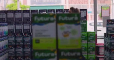 Hırdavatçı dükkanının koridorunda içi dolu raflarla çevrili kıvırcık saçlı bir kadın müşteriye ürün detaylarını gösteriyor.