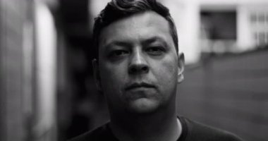 Kentsel sokakta ciddi bir adamın siyah-beyaz yakın çekimi, tarafsız ifade, içsel ruh hali, dramatik monokrom estetik, modern şehrin otantik kişiliği.