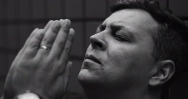 Elleri bağlı dua eden adam, gözleri kapalı, umutsuzluk içinde umut ve rehberlik arayan, inanç, esneklik ve duygusal mücadele içinde, siyah ve beyaz