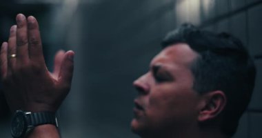 Elleri bağlı dua eden, yukarı bakan, zor zamanlarda umut ve rehberlik arayan, inanç, esneklik ve duygusal mücadeleyi yakından ileten bir adam.