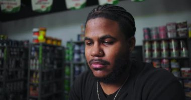 Düşünceli ve düşünceli bir erkek boyacı tezgahın arkasında oturuyor, elleri, organize çalışma alanındaki boya kutuları ve malzemelerle kaplı.