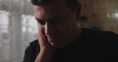 Adamın yüzü dinleniyor, dalgın ve düşünceli bir ifadeyle kameradan dışarı bakıyor, sakin bir ortamda düşünceli bir kaygı ve iç gözlem yansıtıyor.