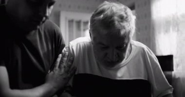 Yaşlı bir adama bunama ya da yaşla ilgili bir hastalıkta yardım eden bir adam mutfakta, nazik bir şekilde omuz omuza, şefkat ve bağlantı gösteren, siyah ve beyaz