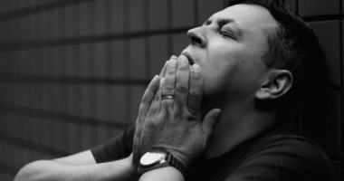 Duygusal bunalımda olan adama yakın çekim, sımsıkı tutulmuş ellerle duvara yaslanma, yoğun zihinsel mücadele, depresyon, iç karışıklık, derin umutsuzluk ve acı, siyah ve beyaz