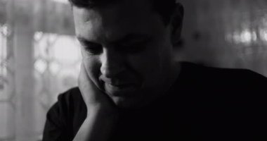 Siyah ve beyazlı bir adam, yüzü üzerinde dinlenen bir el, dalgınlık ve esneklik karışımı ile mesafeye bakıyor, derin düşünce ve ince duygusal gerilim ifade ediyor