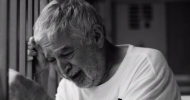 Yaşlı bir adam kafasını pencere korkuluğuna yaslıyor, duygusal yorgunluk ve keder ifade ediyor, kapalı bir umutsuzluk anında gözleri kapalı, siyah ve beyaz