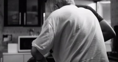 Yaşlılara bunama ya da yaşlılığa bağlı bir hastalığa sahip bir adamın mutfakta oturup fiziksel destek ve bakım sağlaması, şefkat ve bağlantıyı vurgulaması, siyah ve beyaz