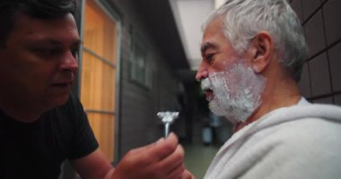 Koridorda jiletle oğlundan yardım alan yaşlı bir adam bakım, şefkat ve aile bağını vurguladı.