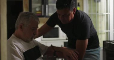 Oğlu, yaşlı babasına bunama ya da yaşla ilgili hastalıklarda yardım ediyor. Kalkıyor ve mutfağa doğru yürürken onlara destek oluyor.