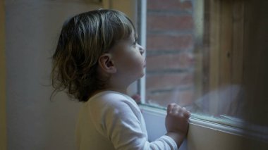 Toddler child staring outside standing by window at home