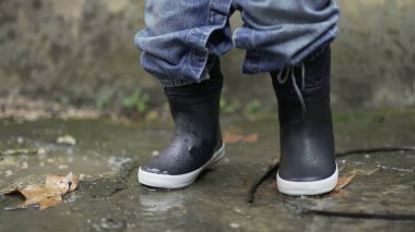 Child jumping into water puddle. Toddler wearing boots splash into puddle