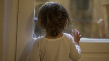 Toddler child staring outside standing by window at home