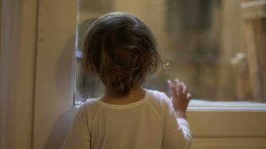 Toddler child staring outside standing by window at home