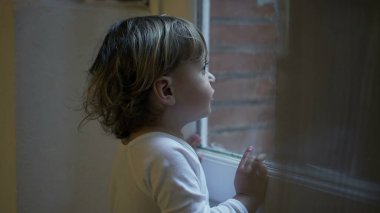 Toddler child staring outside standing by window at home