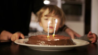 Mother celebrating toddler son birthday, child celebrates two years of age, happy parent with her son