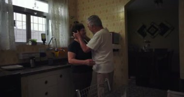 Mutfakta sımsıkı sarılan yaşlı bir çift, içten bir bağ ve sevgi, günlük hayatta samimi ve duygusal bir aşk tasviri.