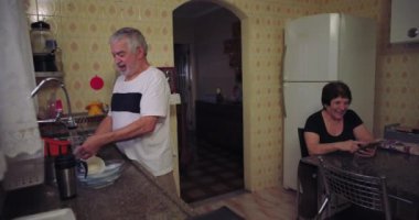 Mutfakta kıdemli bir çift, lavaboda bulaşık yıkayan bir adam ve akıllı telefon kullanan bir kadın.