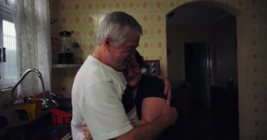 Mutfakta kucaklaşan yaşlı bir çift, şefkat ve şefkat gösteriyorlar, samimi ve samimi bir an, günlük aşk ve bağ kuruyorlar.