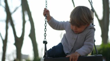 Çocuk parkta, salıncakla oynuyor.