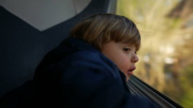 Çocuk trenle seyahate çıktı, pencereye yaslandı.