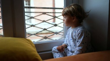 Pencerenin kenarında oturan çocuk dışarı bakıyor. Bebek pencere kenarında oturur.