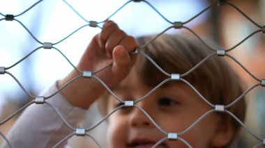 Çocuk oyun bahçesinde metal tel çitlere tutunuyor.