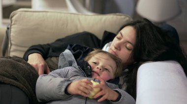 Yorgun anne kanepenin üzerinde küçük çocuğun yanında uyukluyor.