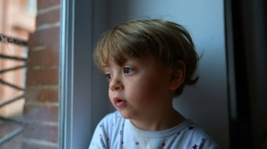 Pencere kenarında hayal kuran çocuk dışarı bakıyor.