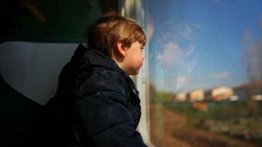 Çocuk trenle seyahate çıktı, pencereye yaslandı.
