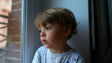 Pencere kenarında hayal kuran çocuk dışarı bakıyor.