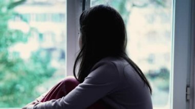 Pencere kenarında oturan 8 yaşında düşünceli bir kız. Düşünceli bir şekilde bakıyor.