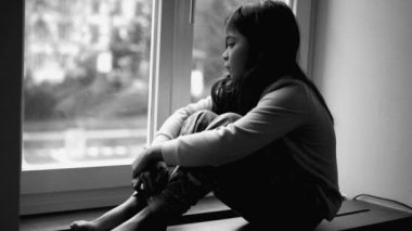 Depresyondaki küçük kız pencerenin kenarında endişeli ve endişeli bir şekilde daireden siyah beyaz, tek renkli manzaraya bakıyor. Yalnız üzgün çocukluk