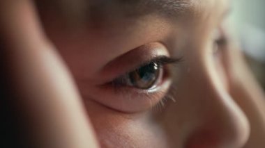 Yumuşak odaklı bir çocuğun gözüne yakın çekim, merakla ve yansımayla çevreyi gözlemlemek, çocukluk içgüdü ve farkındalığının sessiz bir anını yakalamak.