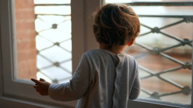 Pencere kenarında oturan küçük çocuk dışarı bakıyor. Çocuk sabah oturur.