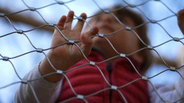 Küçük çocuk oyun bahçesindeki metal çitlere yaslanıyor.