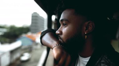 Düşünceli genç bir zenci balkonda metal çubuğa yaslanmış derin zihinsel yansımasına bakıyor. Afrika kökenli düşünceli birinin düşünceli yakın plan yüzü.