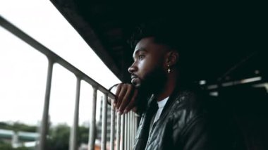 20 'li yaşlarda, Balkona yaslanmış, Derin Düşüncelere dalmış dalgın bir siyah adam. Düşünceli Afrikalı Amerikalının şehir görüşüne bakan iç gözlemci bakışları