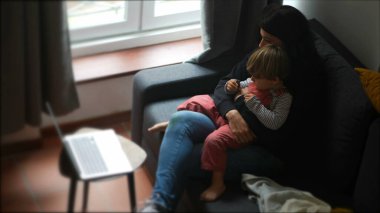 Anne ve çocuk birlikte kanepede oturup evdeki dizüstü bilgisayardan medyanın içeriğini izliyorlar.