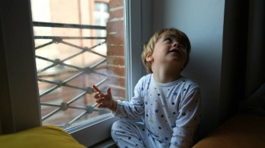 Sabahları pencerenin kenarında oturan küçük çocuk dışarı bakıyor ve elleriyle işaret ediyor.