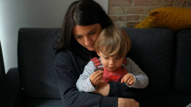 Anne ve küçük çocuk evdeki kanepede oturup kucaklaşıyorlar.