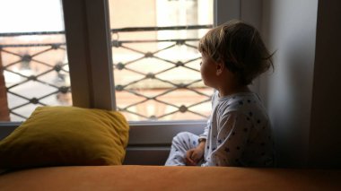 Küçük çocuk pencerenin kenarında oturuyor ve sabahları dışarı bakıyor.