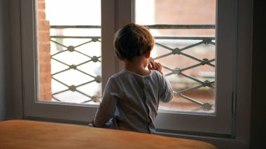 Küçük çocuk pencerenin kenarında oturmuş dışarıya bakıyor.