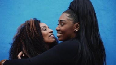 Afrikalı Amerikalı ergen kız annesine sevgiyle sarılıyor. Mavi şehir duvarında ebeveynler ve çocuklar arasında önemli bir an. Aşk ve sevgi