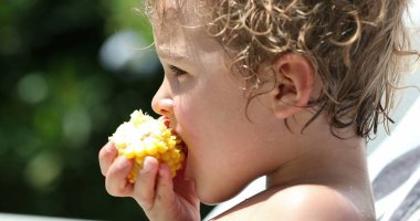 Baby boy eating corn outside